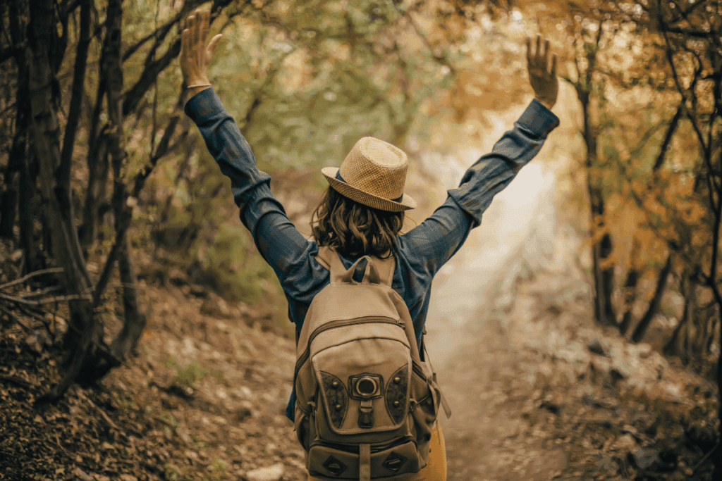 foto de uma mulher caminhando em uma trilha, com mochila nas costas e braços abertos.