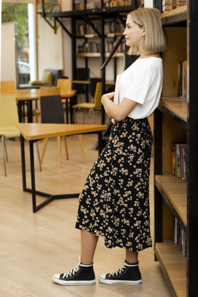 mulher com saia midi floral, camiseta branca e tenis. moda boho chic cm toques de rock.